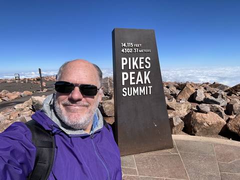      Person standing near a summit sign with a view of the sky.
  