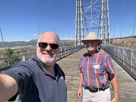 Two men standing on a suspension bridge.