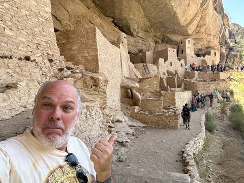       Man in front of cliff dwellings.
  