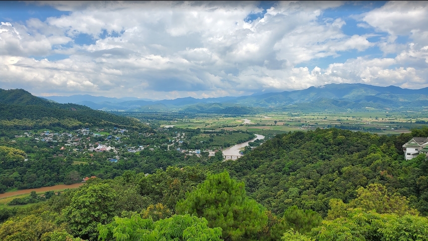       A panoramic view of a valley with a river and mountains in the background.
  