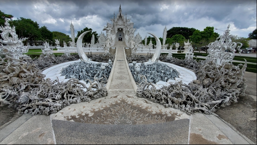       Artistic white temple with intricate details under cloudy skies.
  