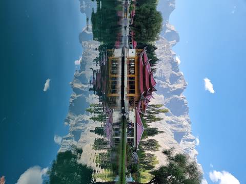 Reflective lake with a traditional building and mountains in the background.