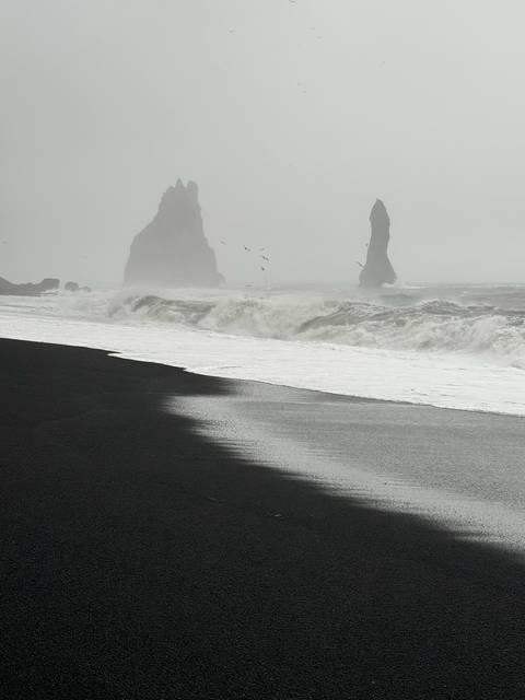 Black sand beach with sea stacks in the distance.