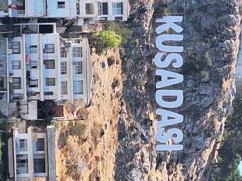 Sign for Kusadasi with mountain and buildings in the background.