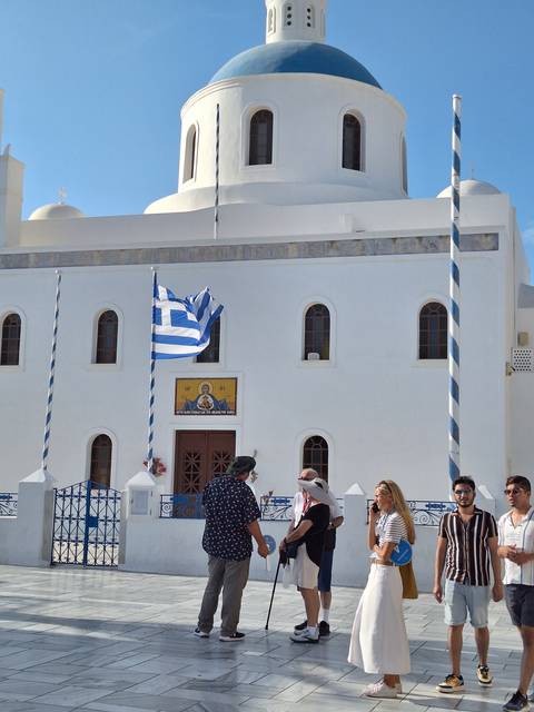 People at a church with Greek flag and clear sky.