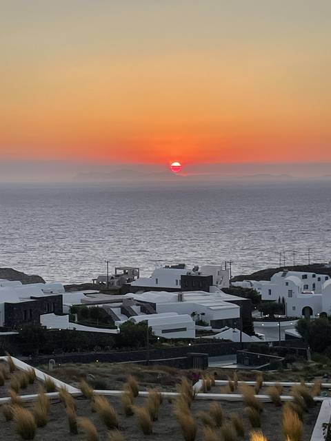       A scenic sunset view over the sea with white buildings on a hillside, possibly in Greece.
  