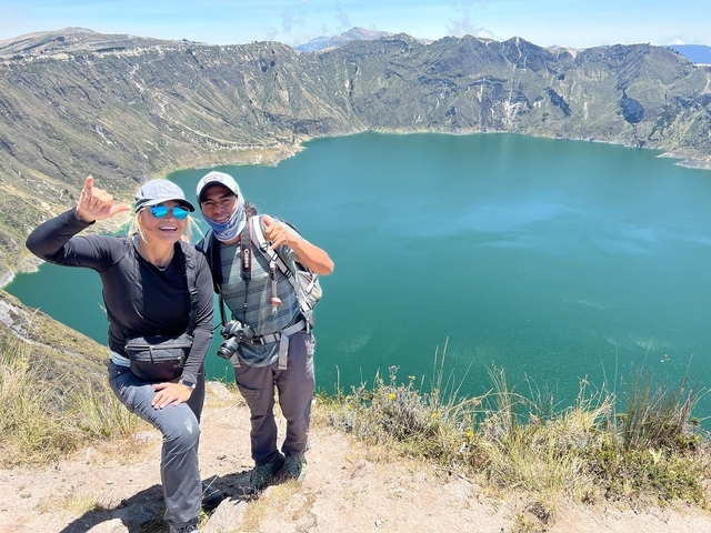       Two people posing with a view of a crater lake behind them.
  