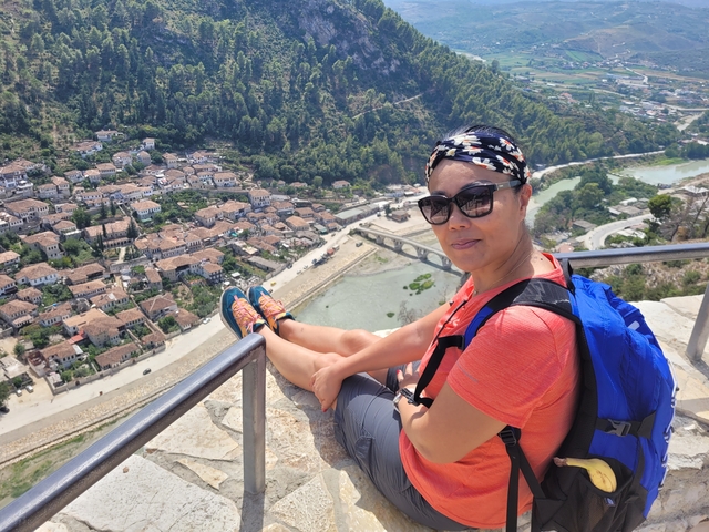       Woman sitting on a railing with an elevated view of a town below.
  