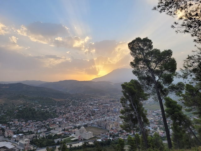 Sunrise view over a city with a mountain in the background and clouds in the sky.