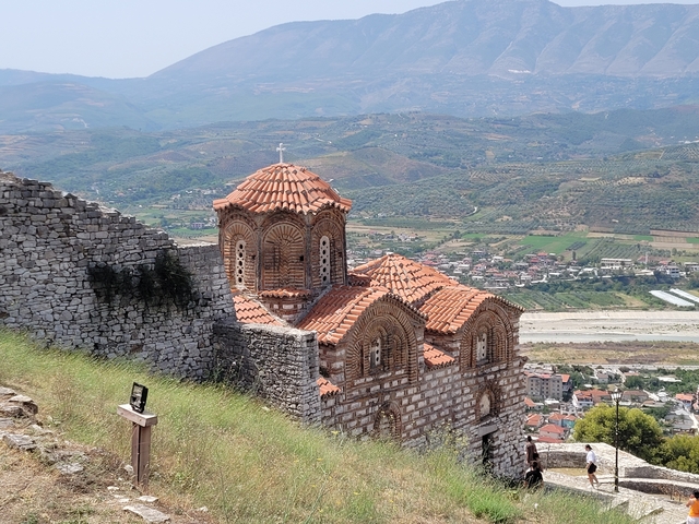       Historic Orthodox church with a scenic backdrop of mountains and a town.
  