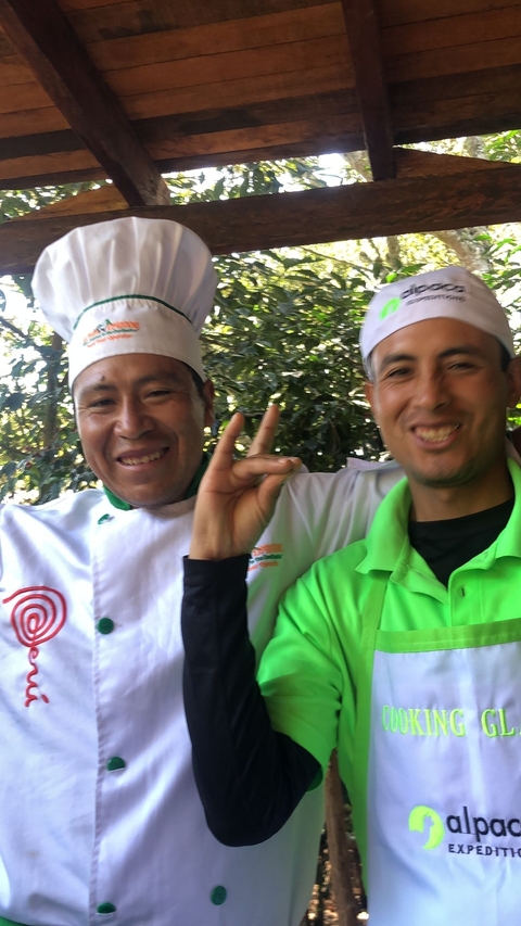 Two men smiling, wearing a chef's hat and outdoor attire.