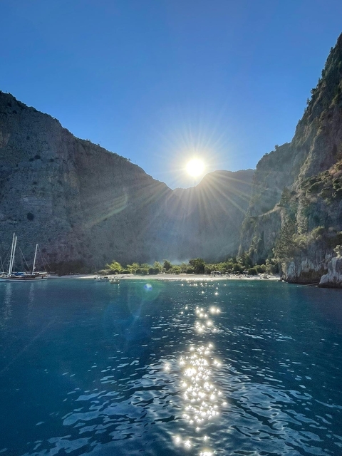 Sun shining over a mountainous bay with boats and a beach.