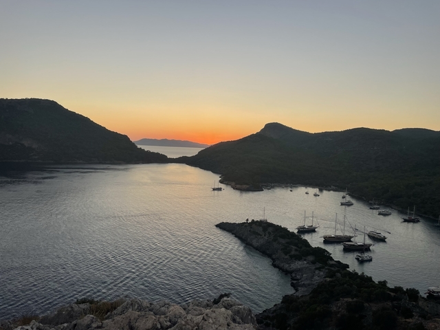 Sunset over a serene bay with yachts and hills.