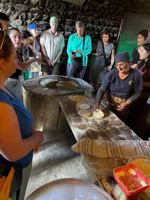 People watching traditional bread-making in a rustic setting.