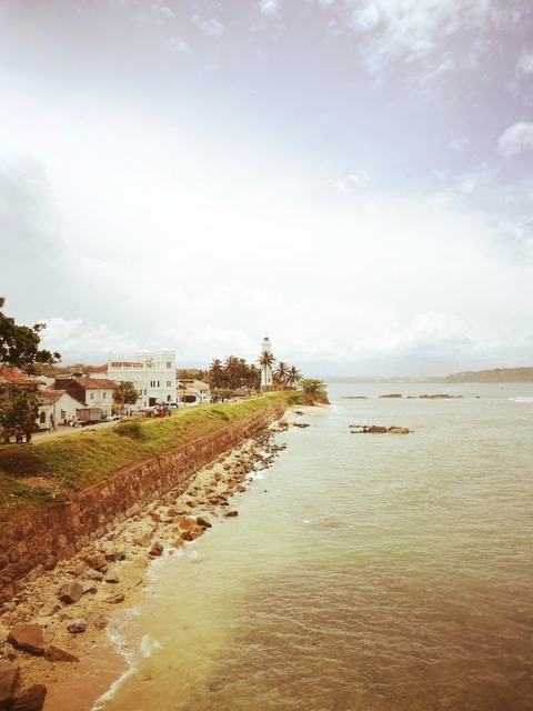       Colonial buildings and a lighthouse by the sea.
  