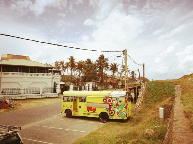 Colorful street bus with palm trees and colonial buildings.