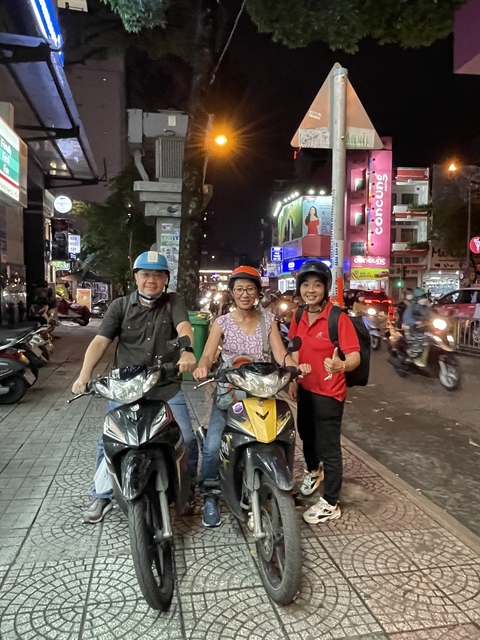 Three people on motorbikes in a bustling city street at night.