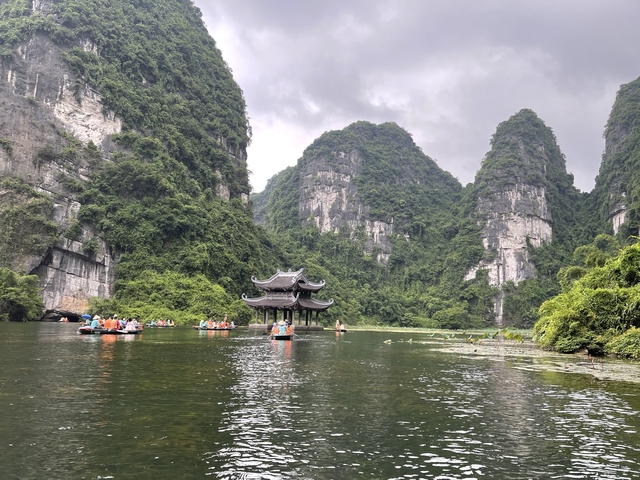 Tourists in boats amidst rocky green mountain scenery.