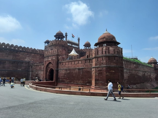       A large red fort with tourists and Indian flag flying.
  