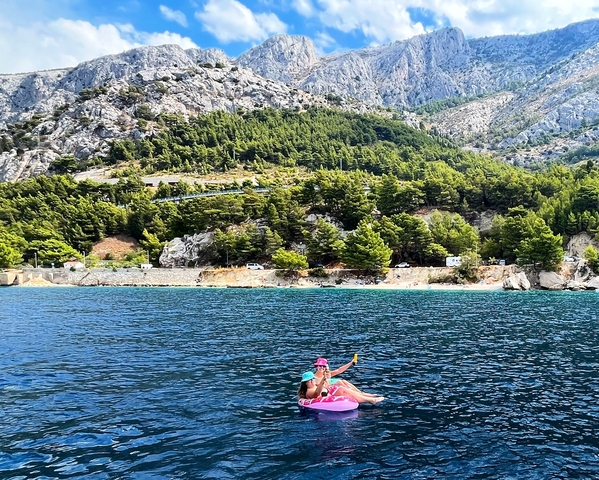People in an inflatable float on a blue body of water with mountainous backdrop.