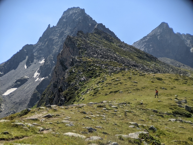A hiker with a backpack on a grassy ridge with rugged mountains in the background.