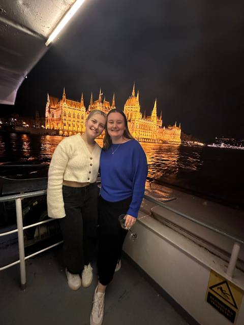 Two people standing on a boat with a lit building in the background.