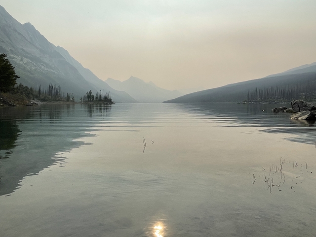 Serene lake view with a smoky atmosphere and distant mountains.