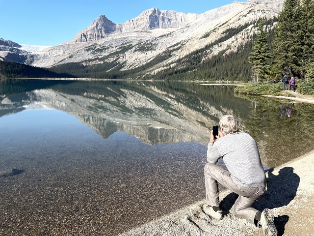Reflection of mountains in a clear lake with a person photographing the scene.
