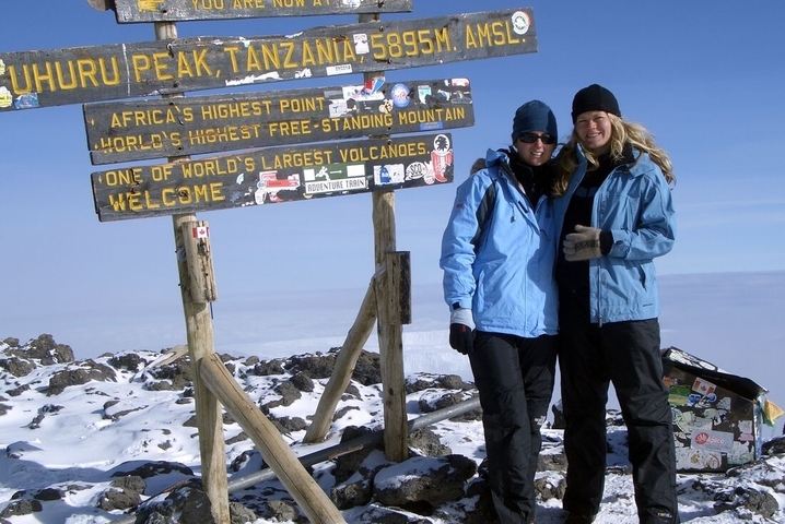 Two people posing at Uhuru Peak, Mount Kilimanjaro, wearing winter gear.