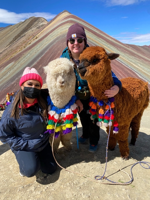 People posing with colorful alpacas at Rainbow Mountain.