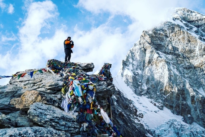       Person on a rocky summit with prayer flags.
  