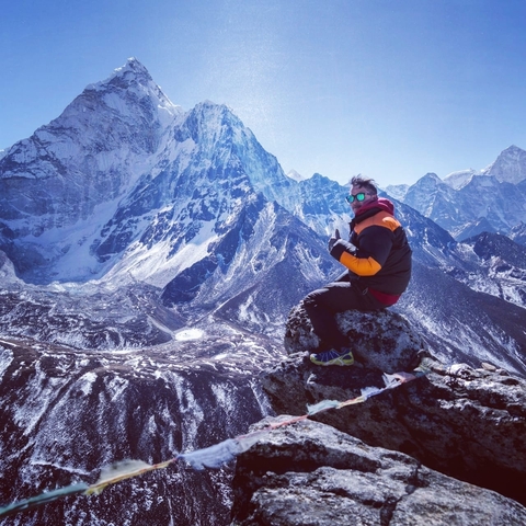       Person sitting on a rocky peak with mountains.
  