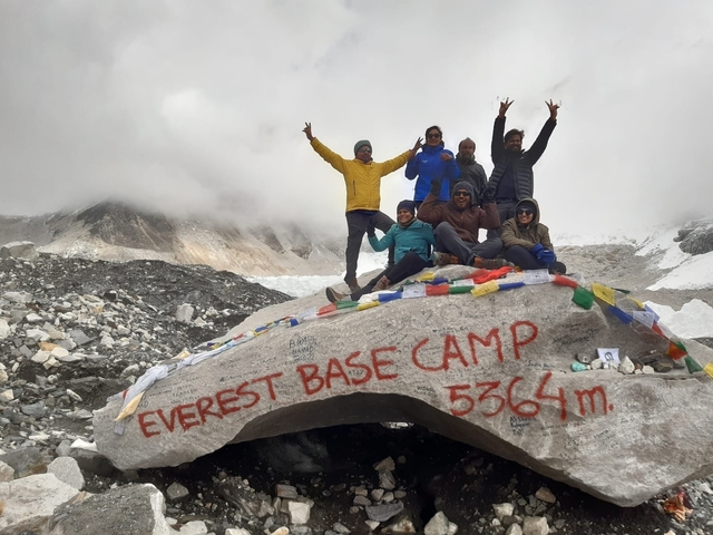       Group of travelers at Everest Base Camp with celebratory pose.
  