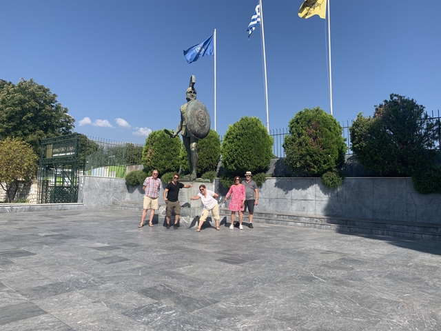       Group of people posing by a statue of a Spartan warrior.
  