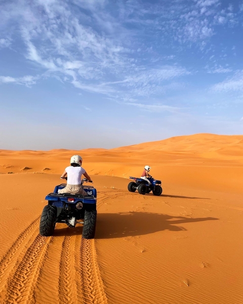 Two people riding quad bikes in a desert.