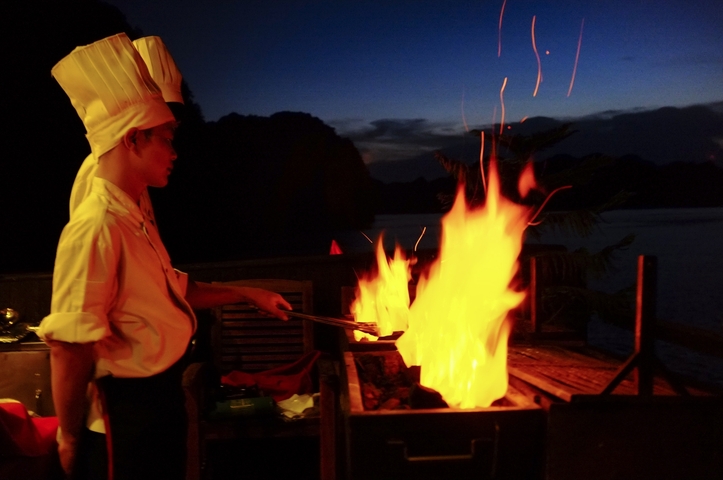 Chef preparing food on a grill with flames at night.