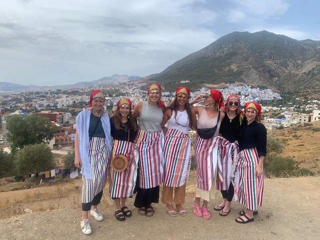       Group of women in traditional attire with a panoramic view of a mountain town.
  