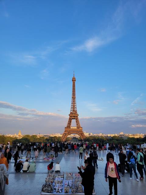 Eiffel Tower with a crowd of people and street vendors, sunny sky.