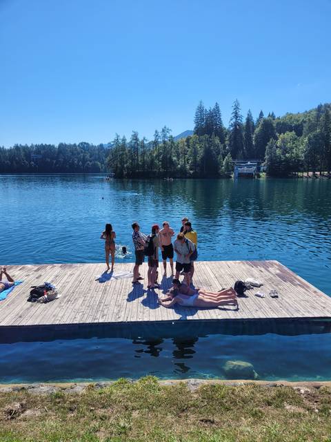 People lounging on a dock by a lake surrounded by trees.