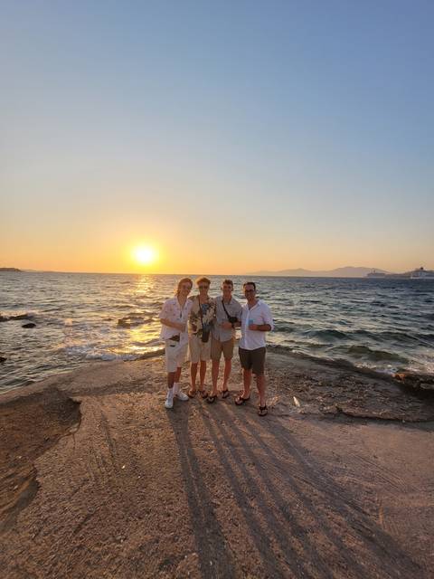 Four people standing together at sunset on a beach.