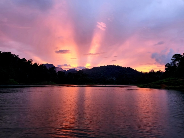 Vibrant sunset over a lake with hills and trees silhouette.