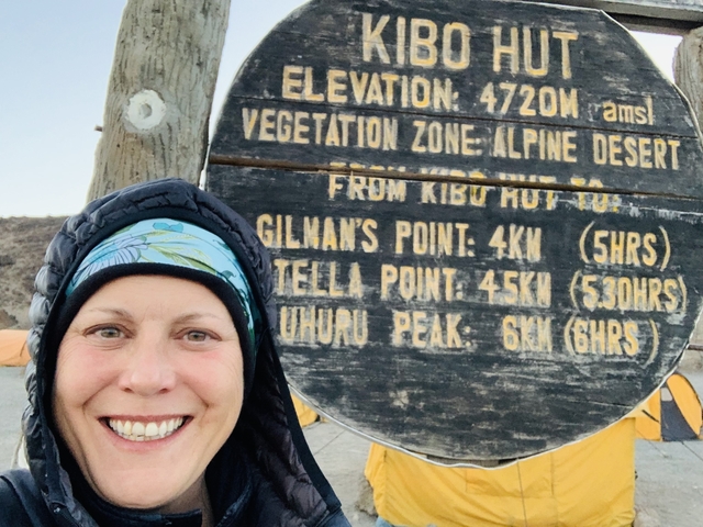       Smiling person in front of a wooden elevation sign.
  