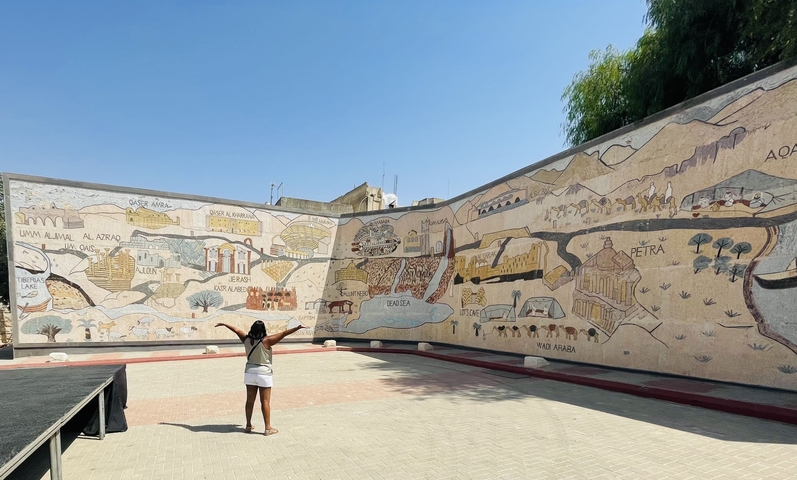       Woman with arms raised in front of a large mural.
  