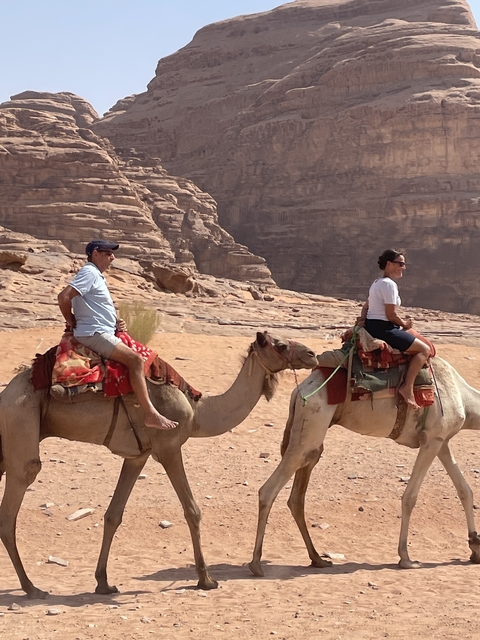       Two people riding camels in a desert landscape.
  