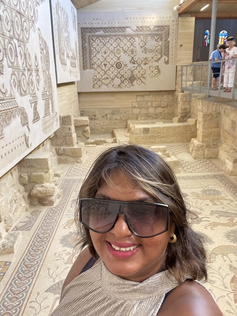       Woman with sunglasses in a room with ancient mosaics.
  