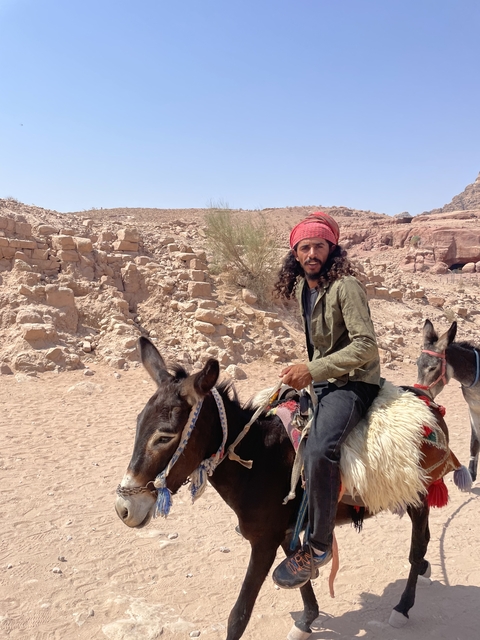 Man riding a donkey in a desert setting.