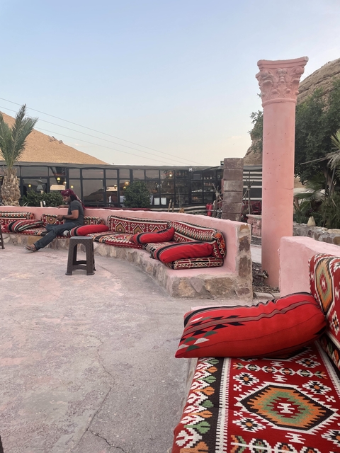       Man sitting on traditional cushions in a courtyard area.
  