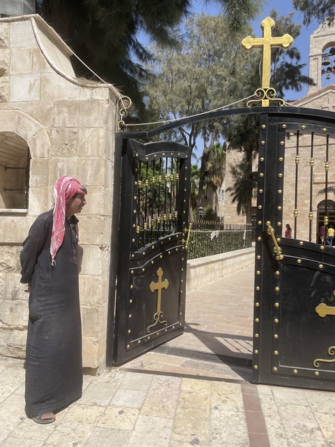       Man in traditional clothes by an ornate gate.
  