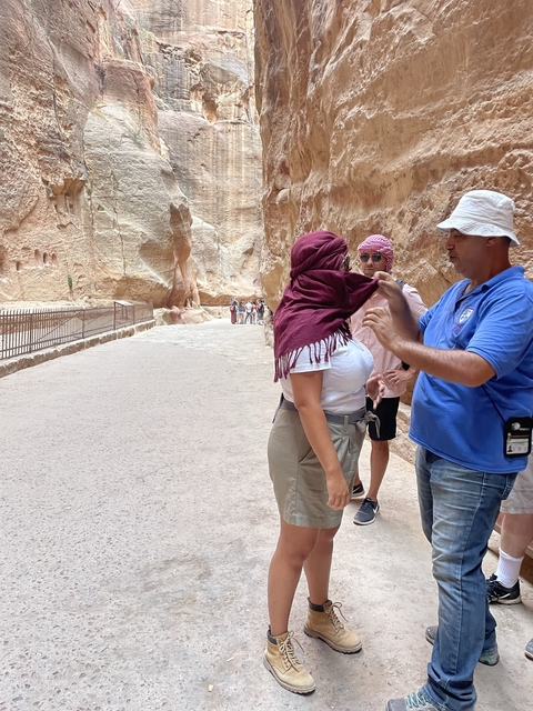       Man helping a woman with a scarf in a canyon path.
  