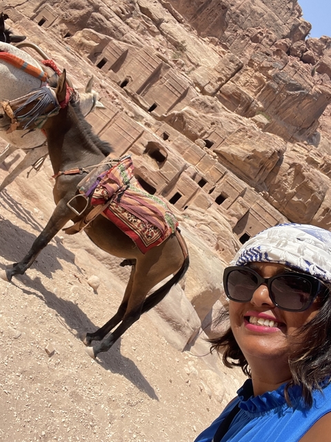       Woman taking a selfie with a donkey in historical setting.
  